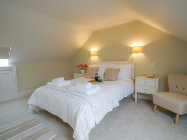 A bedroom with a bed with white bedding and pillows two bedside tables with lamps and a chair at 10 Church Walk  Aldeburgh