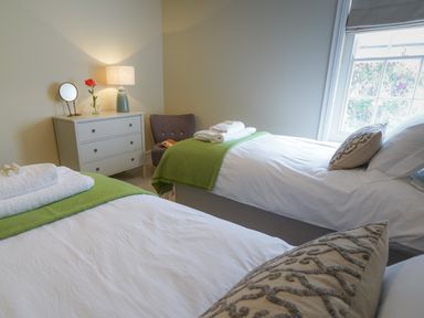 A bedroom with two single beds green blankets and a chest of drawers with a lamp and mirror at 10 Church Walk Aldeburgh