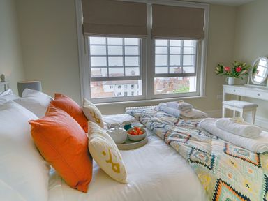 A bedroom with a bed with colorful pillows and folded towels near a window with a city view at 10 Church Walk Aldeburgh