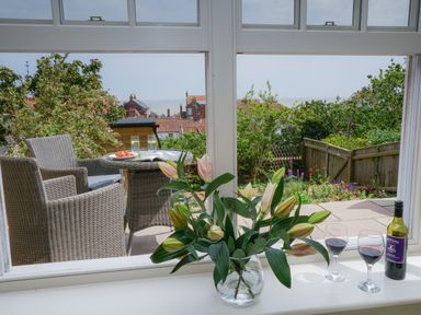 A view through a window showing a patio with a table and two chairs and flowers on the windowsill at 10 Church Walk Aldeburgh