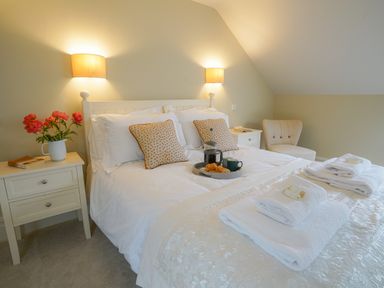 A bedroom with a double bed with white linens and two pillows two bedside tables with lamps a tray with a coffee pot cups and pastries and a beige chair at 10 Church Walk Aldeburgh
