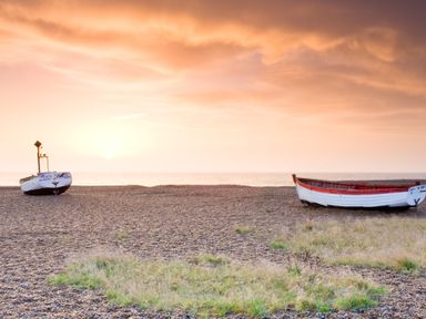 Two boats on a pebble beach near grass patches with the sea and a sunset sky at 10 Church Walk Aldeburgh
