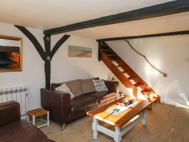 A living room with brown leather sofas wooden coffee table and wooden staircase at 2 Greensleeves in Benhall Near Friston