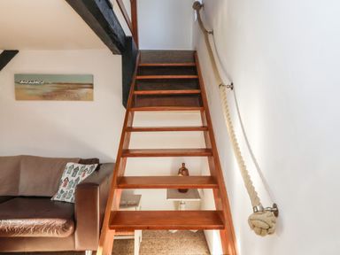 A wooden staircase with rope handrail next to a brown leather couch and a painting on the wall at 2 Greensleeves Benhall Near Friston