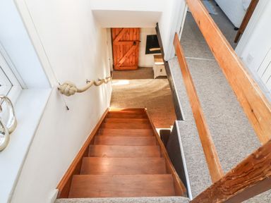 A staircase with wooden steps and a rope handrail leading to a wooden door at 2 Greensleeves in Benhall Near Friston