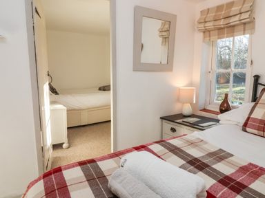 A bedroom with a bed covered in plaid blankets and towels on top a window bedside table with a lamp and a vase and an adjoining room with a bed at 2 Greensleeves Benhall Near Friston