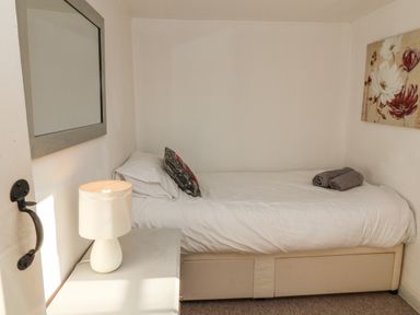 A small bedroom with a single bed white bedding bedside table lamp and a wall mirror at 2 Greensleeves in Benhall Near Friston
