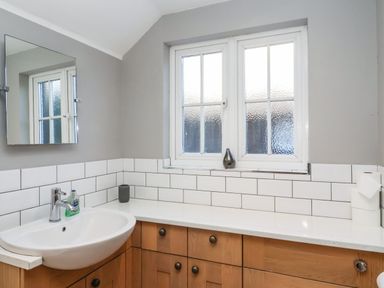 A bathroom with a white sink wooden cabinets a mirror a window and tiled walls at 2 Greensleeves in Benhall Near Friston