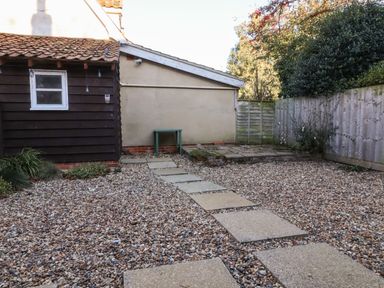 A garden with a gravel ground and stepping stone path next to a building and wooden fence at 2 Greensleeves in Benhall Near Friston