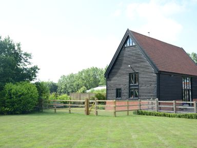 A wooden barn with a red roof next to a fenced lawn and trees at Manor House Barn Peasenhall