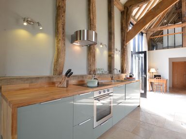 A kitchen with wooden countertops, modern cabinets, built-in oven, and visible wooden beams at Manor House Barn Peasenhall