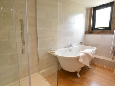 A bathroom with a freestanding bathtub with a towel on it and a glass shower enclosure at Manor House Barn Peasenhall