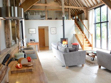 A kitchen and living room area with wooden countertops, gray sofas, a wood-burning stove, and stairs leading to a loft at Manor House Barn Peasenhall