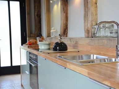 A kitchen countertop with a sink a kettle pots jars knives and a cutting board with bread and pepper at Manor House Barn Peasenhall