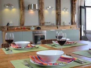 A kitchen with a wooden dining table set with bowls forks spoons striped napkins and glasses of red wine at Manor House Barn Peasenhall