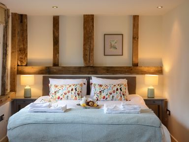 A bedroom with a bed two bedside tables with lamps and wooden beams on the wall at Manor House Barn Peasenhall