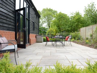 A patio with outdoor seating including a table and chairs next to a house with wooden siding at Manor House Barn Peasenhall