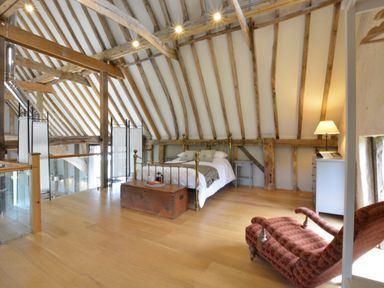 A bedroom with a brass bed wooden chest a chaise lounge and exposed wooden beams at Manor House Barn Peasenhall