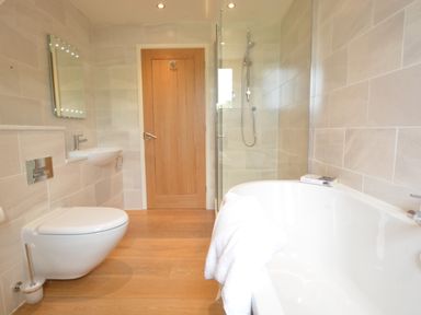A bathroom with a bathtub a shower wall mounted toilet and sink with a wooden door at Manor House Barn Peasenhall