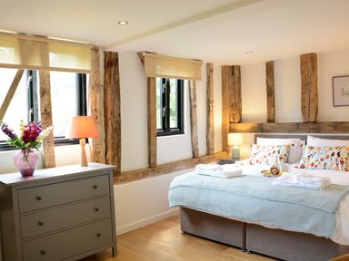 A bedroom with a bed, bedside tables with lamps, a chest of drawers with a lamp and flowers at Manor House Barn Peasenhall
