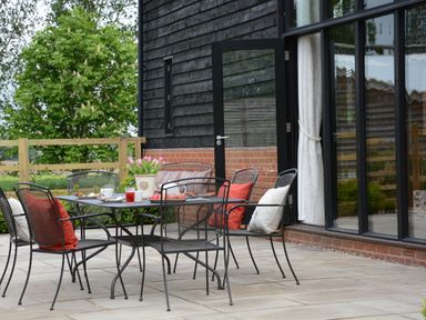A patio with a metal table and chairs with cushions and a pot of tulips outside a building at Manor House Barn Peasenhall
