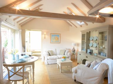 A living room with a dining table, sofa, armchair, cabinet with plates, and a coffee table at The Nookery at Snape Hall in Snape Suffolk