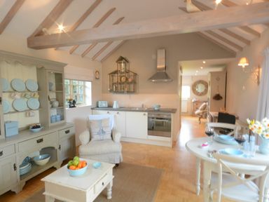 A kitchen and dining area with a cabinet, armchair, table with wine glasses, and pendant lighting at The Nookery at Snape Hall Snape Suffolk