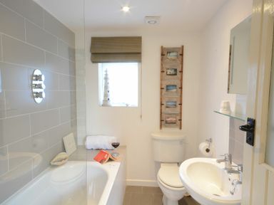 A bathroom with a bathtub sink toilet window with blind and wall decorations at The Nookery at Snape Hall in Snape Suffolk