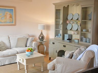 A living room with a sofa armchair coffee table side table and cabinet with plates and cups at The Nookery at Snape Hall in Snape Suffolk