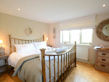 A bedroom with a brass bed frame bedside tables lamps and a dresser under a window at The Nookery at Snape Hall in Snape Suffolk