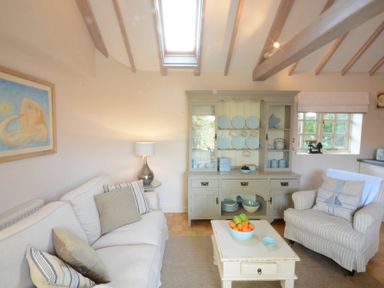 A living room with a sofa, an armchair, a coffee table with fruit bowl, a cupboard with dishes, and a window at The Nookery at Snape Hall Snape Suffolk