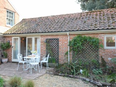 A brick patio with white metal table and chairs and plants on trellises at The Nookery at Snape Hall in Snape Suffolk