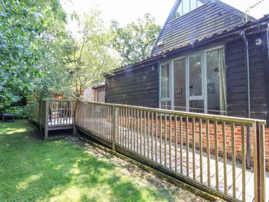 A garden view with grass a wooden deck and railing attached to a house with large windows at Yew Tree Farm Stable Worlingworth
