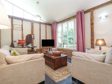 A living room with beige sofas a wooden coffee table pink curtains and a rocking horse at Yew Tree Farm Stable Worlingworth