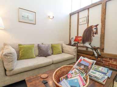 A sitting area with a beige sofa and green and gray cushions a wooden coffee table with magazines and a toy rocking horse in the corner at Yew Tree Farm Stable Worlingworth