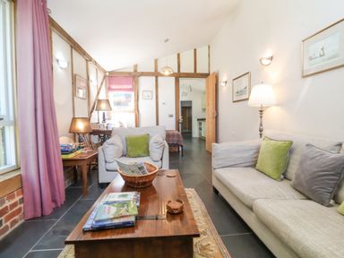 A living room with gray sofas green and gray cushions wooden coffee table and pink curtains at Yew Tree Farm Stable Worlingworth near Framlingham