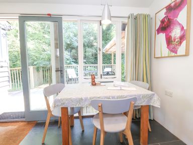 A dining table with four chairs near a glass door leading to a wooden deck with outdoor chairs at Yew Tree Farm Stable Worlingworth
