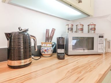 A kitchen countertop with a kettle mug with sticks coffee pod machine microwave and three canisters at Yew Tree Farm Stable Worlingworth near Framlingham