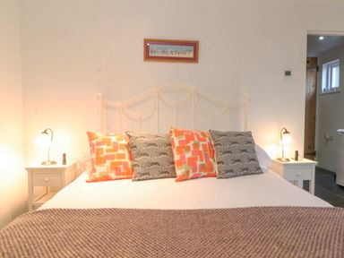 A bedroom with a bed with colorful pillows two bedside tables with lamps and a small framed picture on the wall at Yew Tree Farm Stable in Worlingworth near Framlingham
