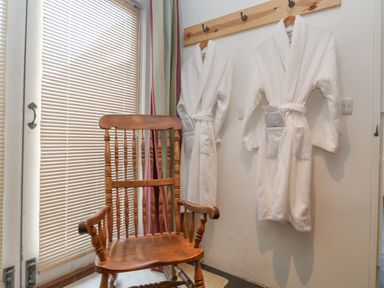 Two white bathrobes hanging on wooden hooks next to a wooden rocking chair in a room
