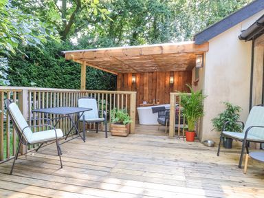 A wooden deck with chairs a table and plants and a covered area with a bathtub at Yew Tree Farm Stable Worlingworth near Framlingham