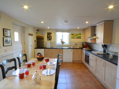 A kitchen with a dining table set with plates cups and glasses and wooden cabinets along the wall at The Cart House in Sudbourne Near Orford