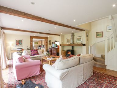 A living room with sofas a wood burning stove and a large rug at The Cart House in Sudbourne Near Orford