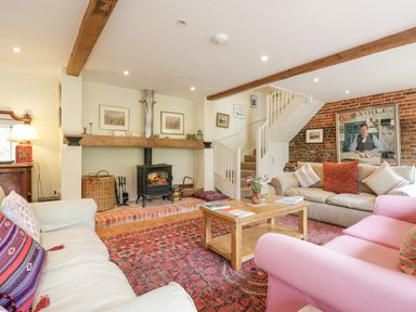 A living room with sofas a wooden coffee table a wood burning stove and a staircase at The Cart House in Sudbourne Near Orford
