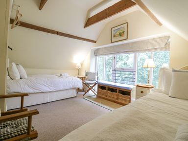 A bedroom with two beds a window bench with baskets and wooden beams on the ceiling at The Cart House Sudbourne Near Orford
