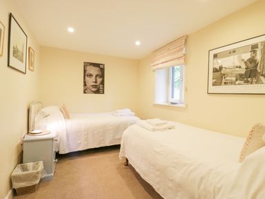 A bedroom with two single beds a window with a blind and framed pictures on walls at The Cart House Sudbourne Near Orford