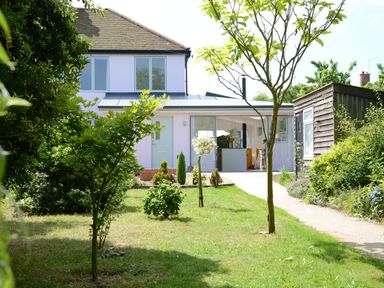 A garden with trees and bushes leading to a house with glass doors and a wooden shed on the right at 2 Pink Cottages Aldeburgh