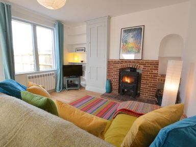 A living room with a fireplace television colorful cushions and a striped rug at 2 Pink Cottages Aldeburgh
