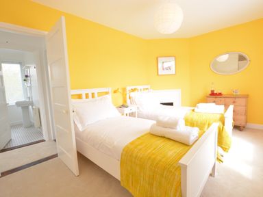 A bedroom with two single beds with yellow throws and white bedding at 2 Pink Cottages Aldeburgh