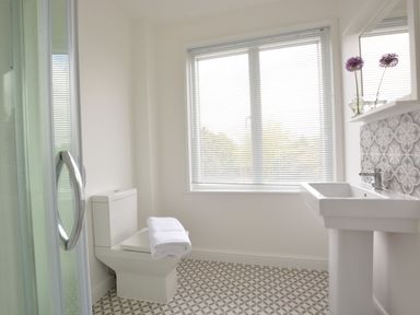 A bathroom with a toilet holding a folded towel a sink with two flowers in vases and patterned floor tiles at 2 Pink Cottages Aldeburgh